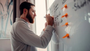 a man writing on a white board with orange markers